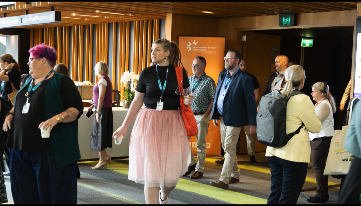 Sandy at an education conference between sessions, in a pink tutu and lanyard, speaking with attendees in a venue corridor.