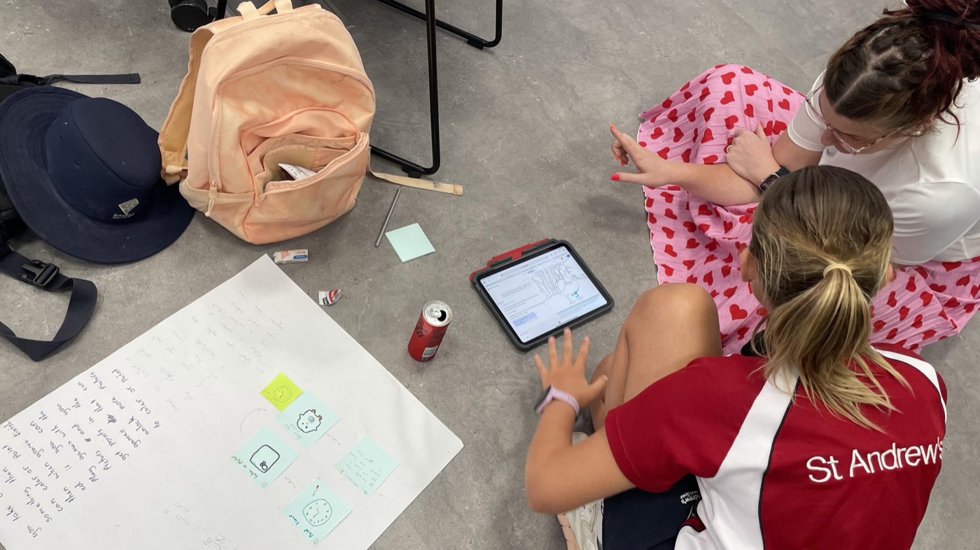 Sandy Robinson working with a student on an iPad alongside hand-drawn UI sketches