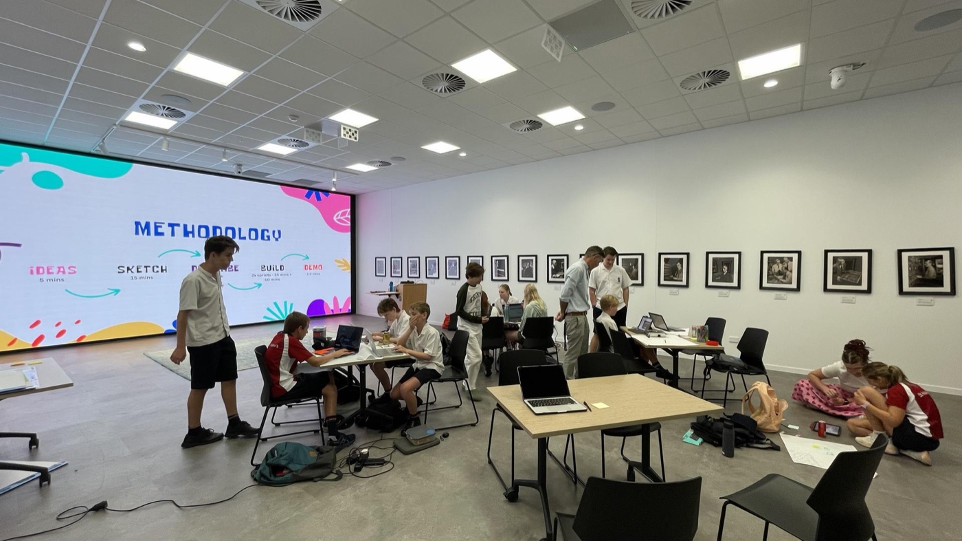 Workshop room with students at laptops during the Kids Vibe Coding Hackathon.